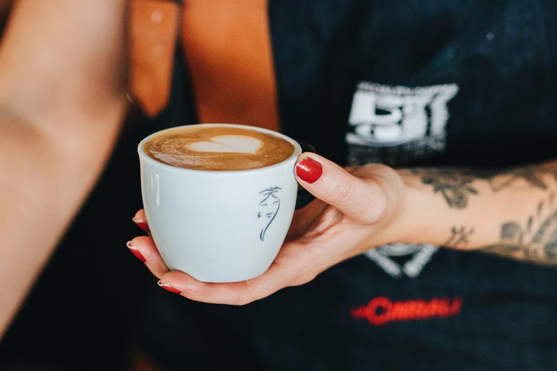 Kvinna på ett café som håller i en cappuccino